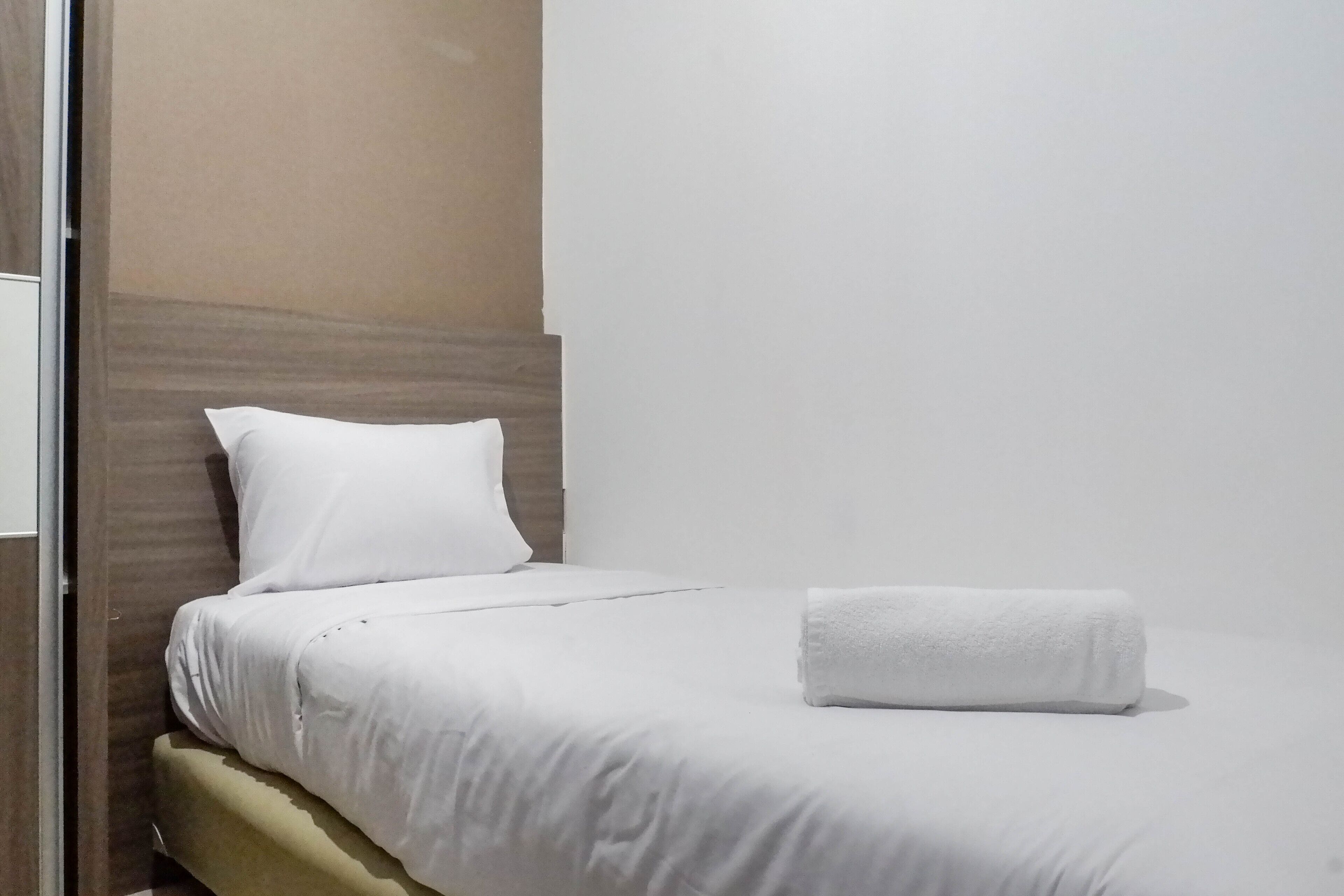 Una cama bien tendida con sábanas blancas y una toalla blanca enrollada al lado.
