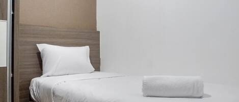 Una cama bien tendida con sábanas blancas y una toalla blanca enrollada al lado.