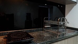 A kitchen with a black induction cooktop, a stainless steel sink, and a dish drying rack. - Best Price 2Br With Pool View Apartment At Taman Melati Surabaya (Surabaya)