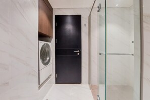 A modern bathroom with a dark door, a glass shower enclosure, and a washing machine. - Fancy And Nice 1Br At Branz Bsd Apartment (Pagedangan)