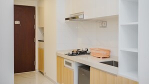 A kitchen with white cabinets, a wooden door, a stove, and a sink. - Cozy Studio Room At Sky House Bsd Apartment (Pagedangan)