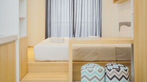 A modern, compact room with a bed, a small table, and a window with curtains. - Cozy Studio Room At Sky House Bsd Apartment (Pagedangan)