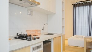 A compact kitchen with a gas stove, sink, and a small countertop. A wooden cabinet and a basket are also visible. - Cozy Studio Room At Sky House Bsd Apartment (Pagedangan)