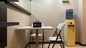 A small hotel room with a white table, a chair, a water dispenser, and a complimentary food and beverage bag. - Comfort And Minimalist 2Br At Maple Park Sunter Apartment (Jakarta)