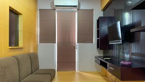 A compact living space with a sofa, a sliding door closet, a built-in TV, and a small kitchen area with a microwave. - Comfort And Minimalist 2Br At Maple Park Sunter Apartment (Jakarta)