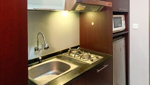 A compact kitchen with a stainless steel sink, gas stove, and a microwave. - Comfort And Minimalist 2Br At Maple Park Sunter Apartment (Jakarta)