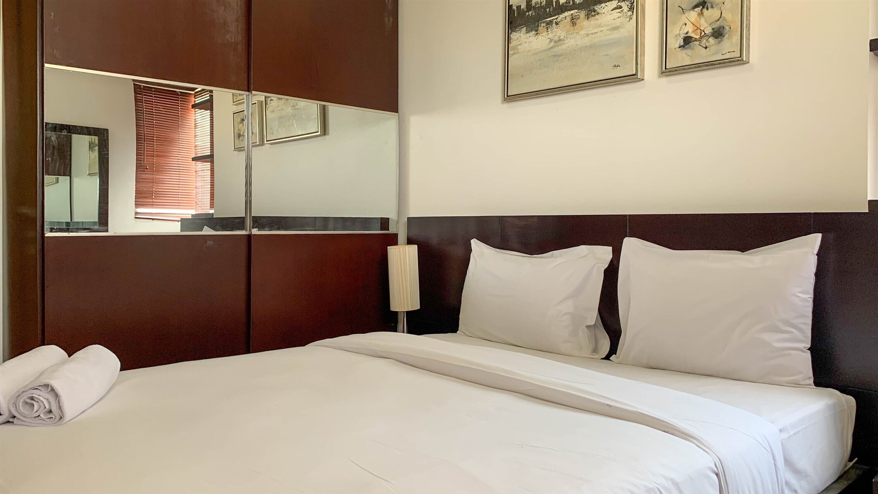Egy szállodai szoba, amelyben egy nagy ágy, egy tükör és két, keretbe foglalt festmény található a falon.