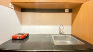 A small kitchen with a black countertop, a stainless steel sink, and wooden cabinets. - Spacious Chic Studio Room Apartment At Gateway Pasteur (Cimahi)