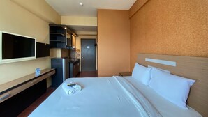 Una habitación de hotel con cama, televisión, una kitchenette pequeña y la puerta del baño.