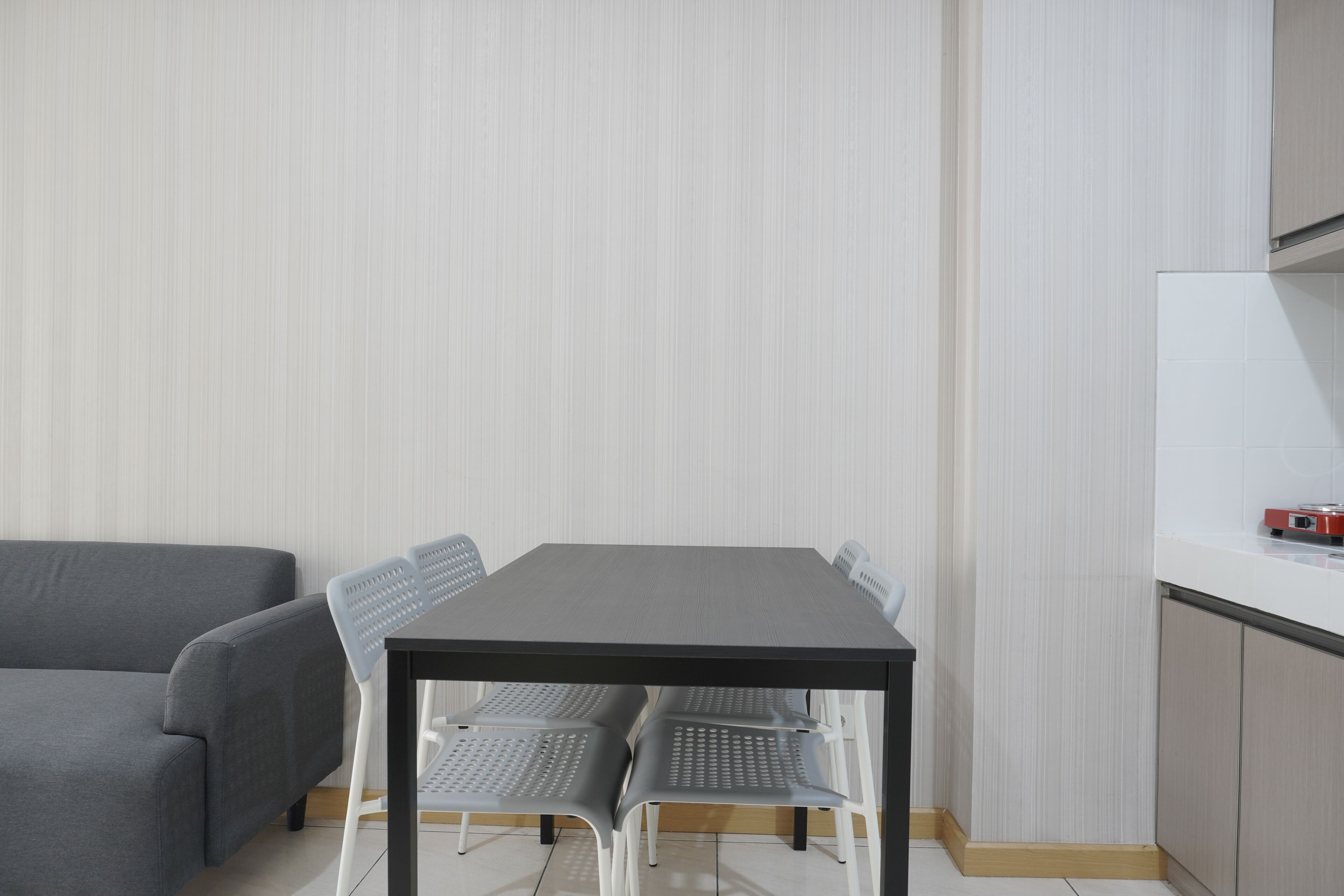 Een moderne keuken met een eettafel en stoelen, een grijze bank en een wit aanrecht.