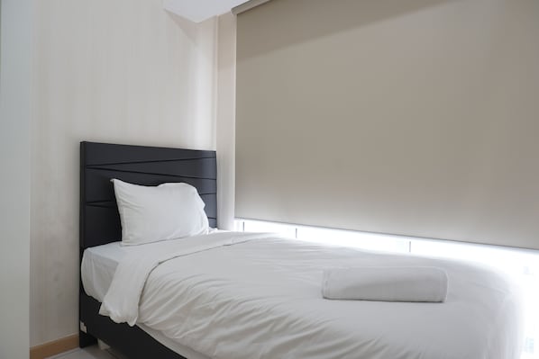 A neatly made bed with white linens and a black headboard in a modern room with a large window.