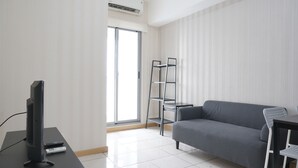 A modern living room with a flat-screen TV, a grey sofa, a small table, and a metal shelf unit.