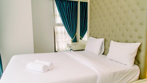 Ein Hotelzimmer mit einem großen Bett, weißer Bettwäsche, einem gepolsterten Kopfteil, einem Nachttisch und einem Fenster mit blauen Vorhängen.