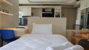 Una habitación de hotel con cama, escritorio, silla y una pequeña kitchenette.