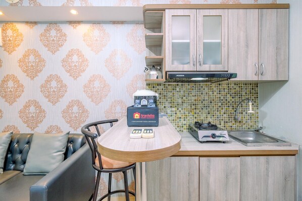 A compact kitchen with a wooden countertop, a gas stove, a sink, and a microwave. There is a seating area with a sofa and a chair.
