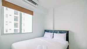 A clean, modern hotel room with a large bed, white linens, and a view of a building through the window. - Comfort And Strategic 2Br At Bassura City Apartment (Jakarta)