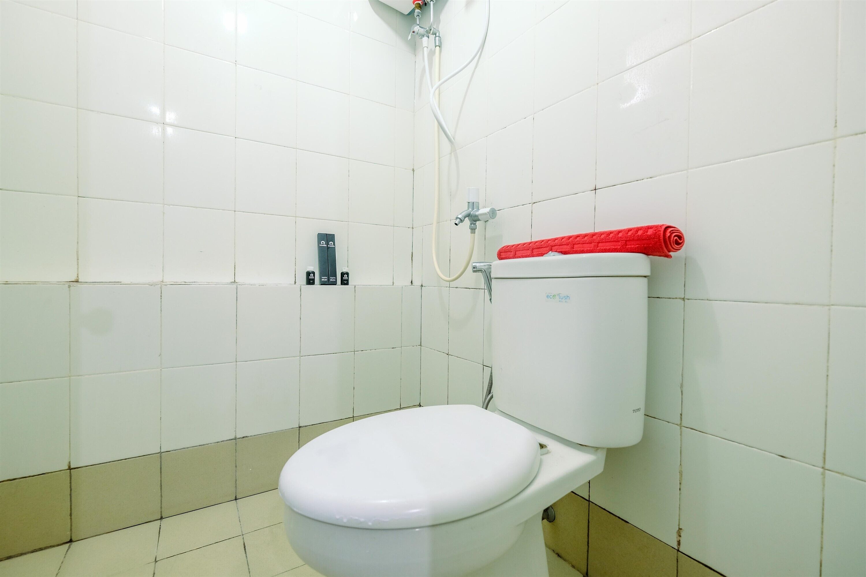 Un inodoro blanco con tapa roja en un baño con paredes y suelo de baldosas blancas.
