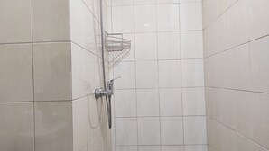 Un espace douche avec des carreaux blancs, une pomme de douche en métal et une étagère en métal.