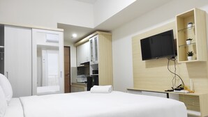 A hotel room with a bed, a TV mounted on the wall, a small kitchen area, and a wardrobe.