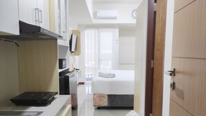 Une chambre d’hôtel compacte comprenant un coin cuisine, un lit, une fenêtre avec des rideaux et une porte en bois.