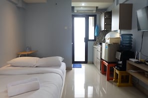 A hotel room with a bed, a small table with a water bottle, a kitchenette with a water dispenser, and a TV mounted on the wall. - Nice And Strategic Studio Kebagusan City Apartment (Jakarta)