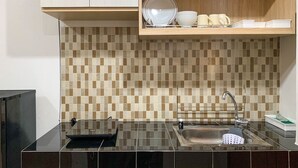 A modern kitchen with a black countertop, a sink, and a tiled backsplash. - Comfort Studio Room At Margonda Residence 5 Apartment (Depok)