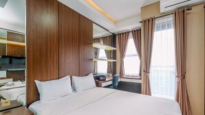 Ein Hotelzimmer mit einem großen Bett, einem Schreibtisch, einem Sessel, einem Fernseher und einem Fenster mit Vorhängen.