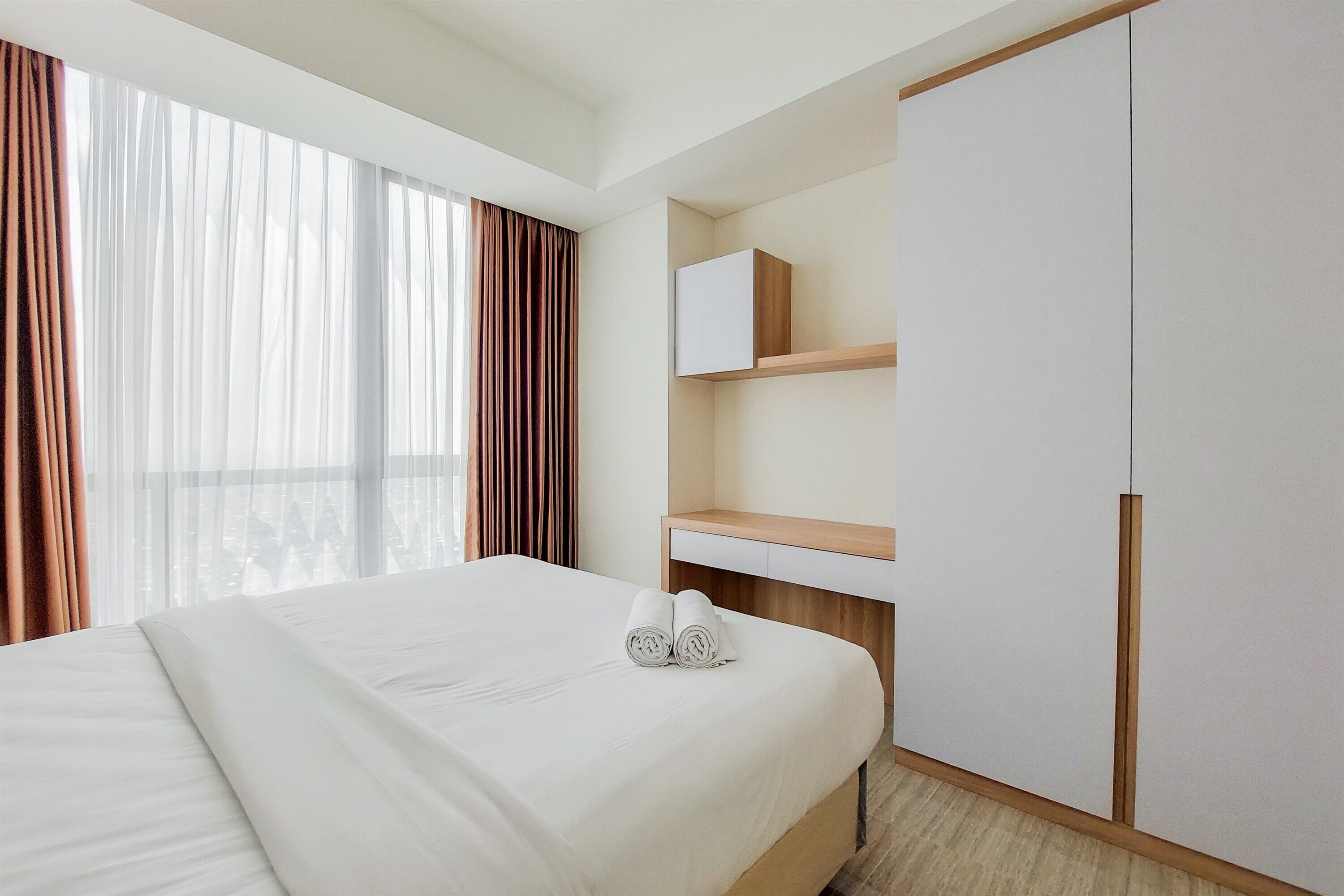 A hotel room with a large bed, a wooden nightstand, a wardrobe, and a window with curtains.