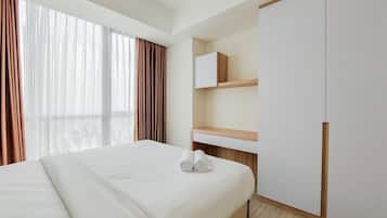 A hotel room with a large bed, a wooden nightstand, a wardrobe, and a window with curtains.