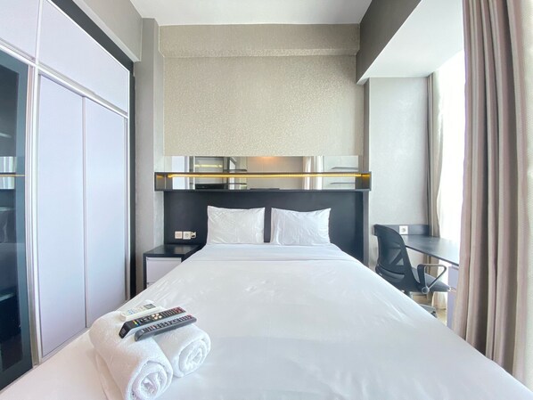 A hotel room with a large bed, a desk, and a wardrobe. - Minimalist And Affordable Studio Apartment At Taman Melati Jatinangor (Hegarmanah)