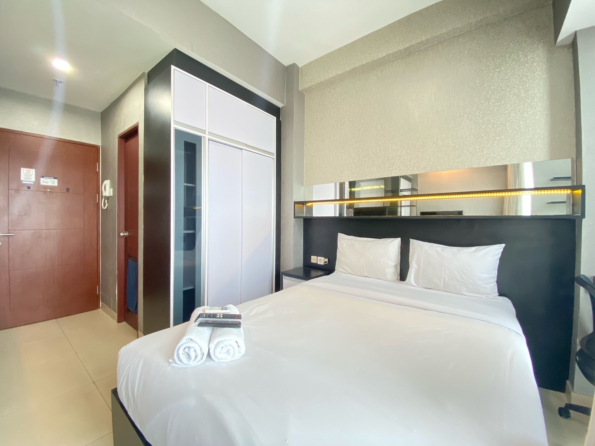 A hotel room with a bed, a wardrobe, a mirror, and a bedside table.