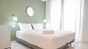 Ein ordentlich bezogenes Bett mit weißen Leinentüchern, ein Nachttisch und zwei Wandleuchten.