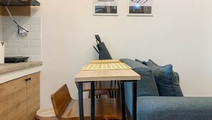 A compact kitchen with a wooden table, a sink, and a countertop. There are two framed pictures on the wall and a grey sofa in the living area. - Comfort And Nice 2Br At Cinere Resort Apartment (Depok)