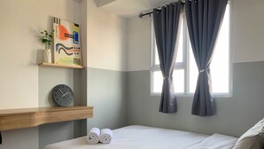 A neatly made bed with white linens, a clock on a shelf, and a painting on the wall. - Comfort And Nice 2Br At Cinere Resort Apartment (Depok)