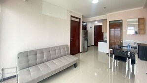 Una sala moderna con un sofá gris, una zona de comedor con una mesa y sillas negras, y una cocina con refrigerador y armarios.