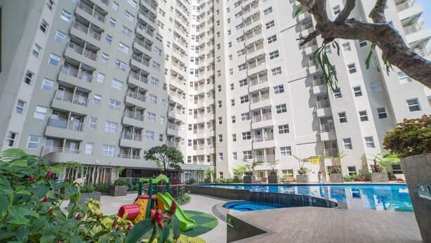 Un edificio residencial de gran altura con varios balcones, piscina y área de juegos para niños.