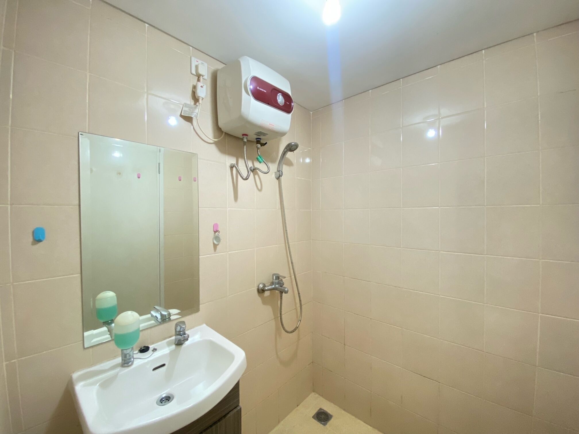 Ein Badezimmer mit weißem Waschbecken, einem Spiegel, einer Handbrause und einem Wandheizkörper.