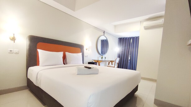A hotel room with a large bed, a bedside table, a mirror, and a window with curtains. - Elegant And Homey Studio At Marquis De Lafayette Apartment (Semarang)
