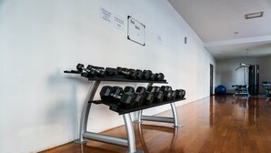 Un gimnasio con un estante de mancuernas, suelo de madera y equipo de ejercicio al fondo.