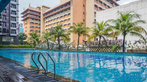 Una piscina con cubierta de madera, rodeada de palmeras y edificios modernos.