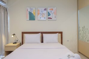 A hotel room with a bed, two pillows, a nightstand with a lamp, and three wall art pieces.
