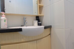 A bathroom with a white sink, a mirror, a wooden cabinet, and toiletries.