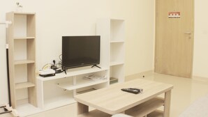 Une pièce avec un téléviseur posé sur un meuble, une petite table et une porte portant un panneau indiquant la sortie de secours.