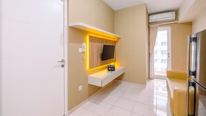 A modern hotel room with a white door, a mounted TV, a bedside table with a lamp, and a sofa. - Well Designed 2Br Apartment At Springlake Summarecon Bekasi (Bekasi)