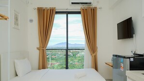 Una habitación de hotel con cama, televisor, refrigerador y ventana con cortinas.