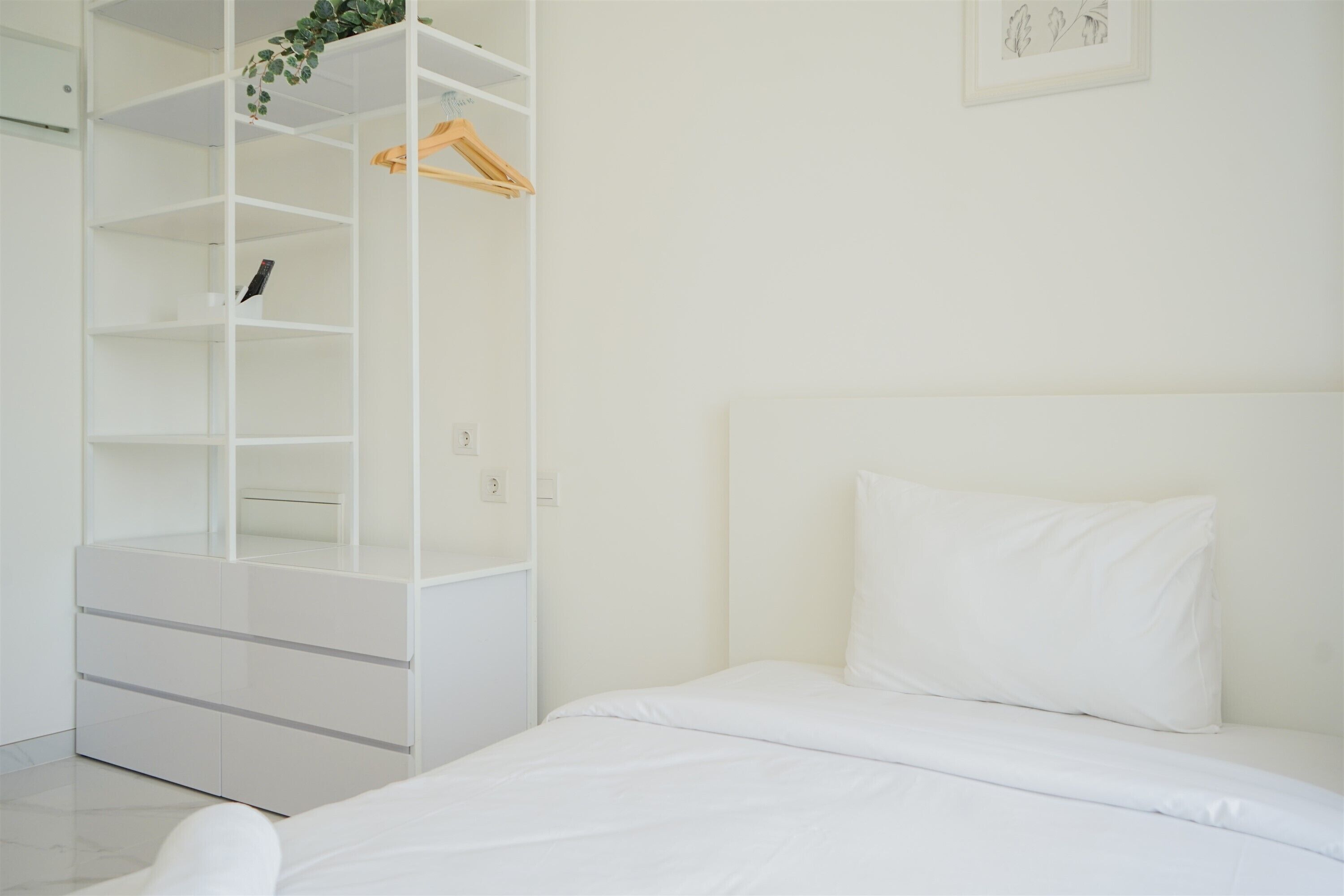 A bedroom with a white bed, a white wardrobe, and a white shelf unit.