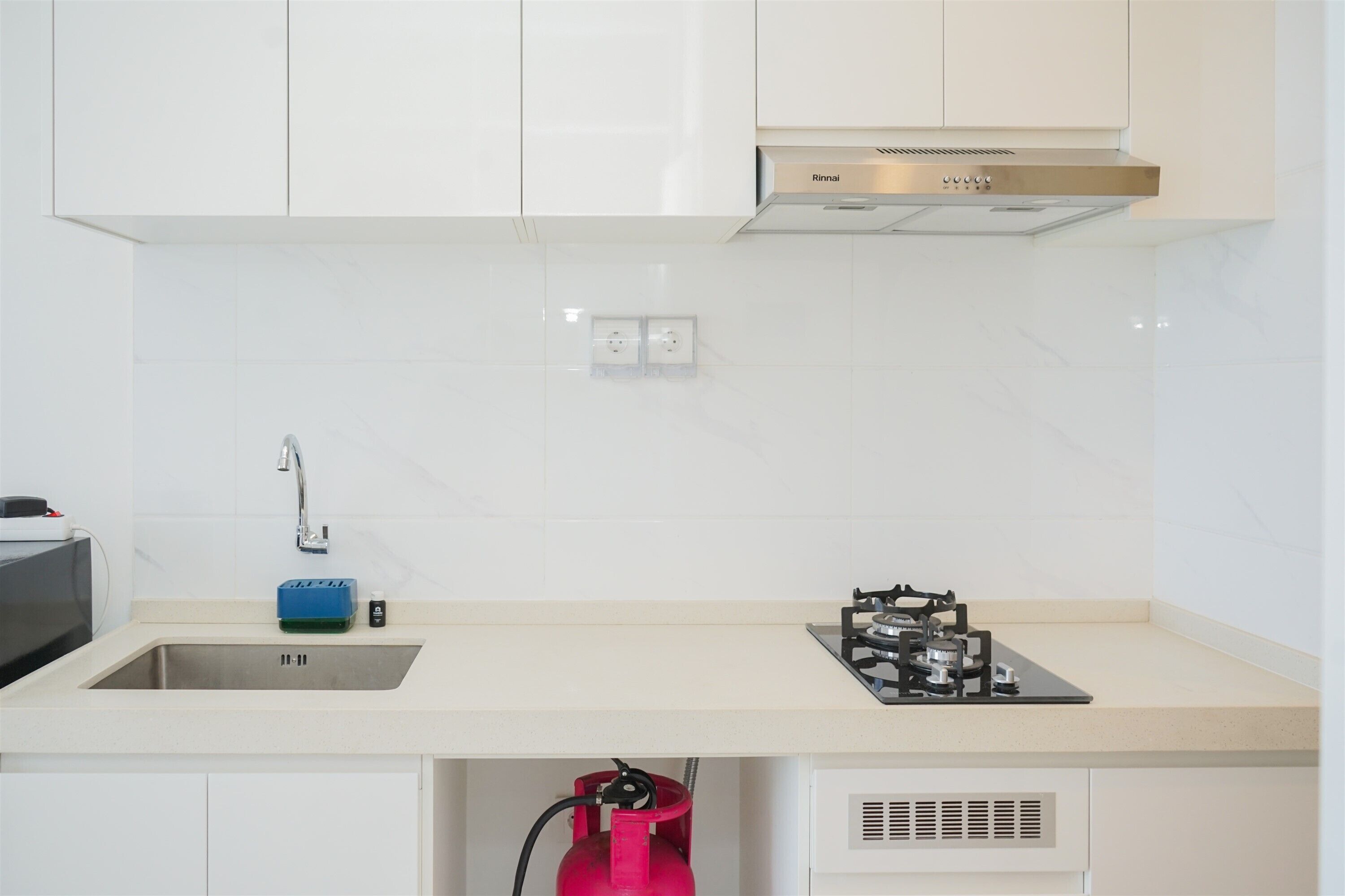 Una cocina moderna con armarios blancos, un lavamanos de acero inoxidable, una estufa a gas y un cilindro de gas rojo.