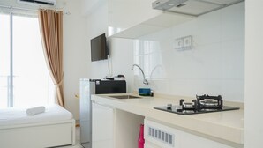 Una habitación de hotel compacta con cama, kitchenette, televisor y ventana con cortinas.