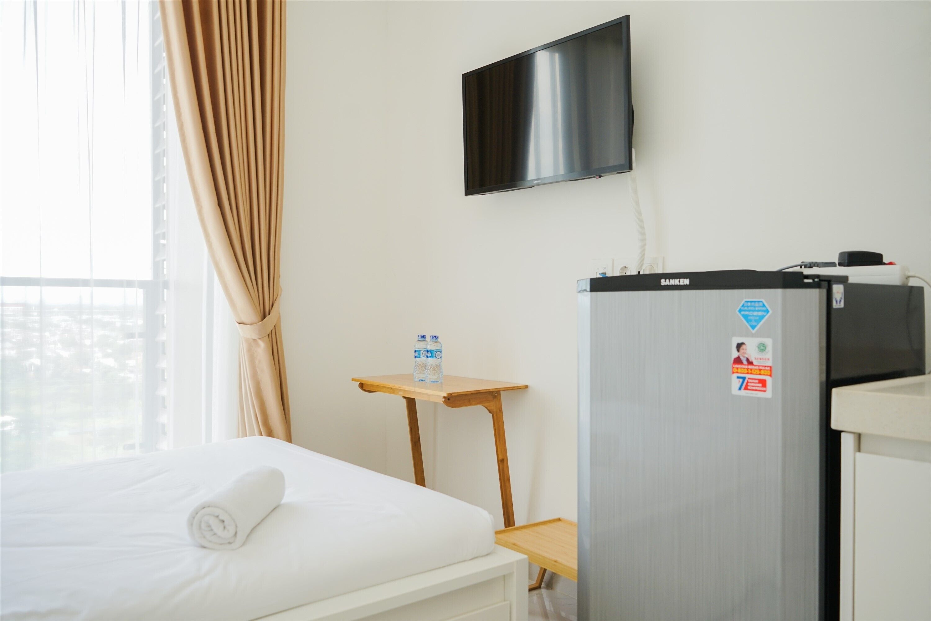 A hotel room with a bed, a television mounted on the wall, a minibar, and a water dispenser.