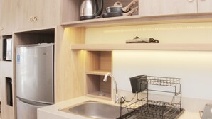 A modern kitchen with a stainless steel refrigerator, a sink with a dish rack, and wooden cabinets. - Minimalist And Cozy Studio At Vasanta Innopark Apartment (Cikarang)